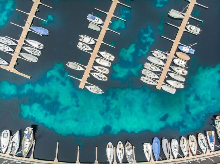 Aerial view of a vibrant marina with boats filling marina slips along multiple piers, set against stunning turquoise blue water. Fill your empty slips fast with Marina Moorage