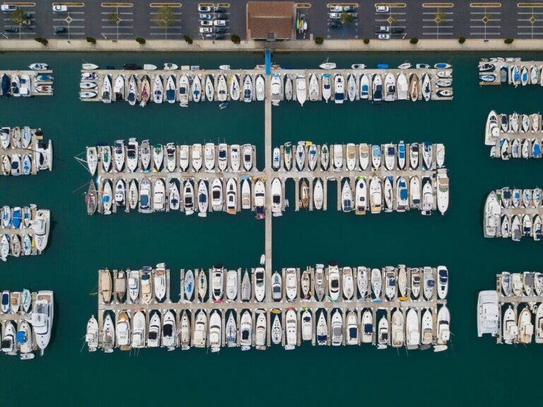 Aerial view of a marina with multiple rows of docked boats, showcasing ample seasonal boat moorage and a parking lot at the top of the image. Fill your empty slips fast with Marina Moorage