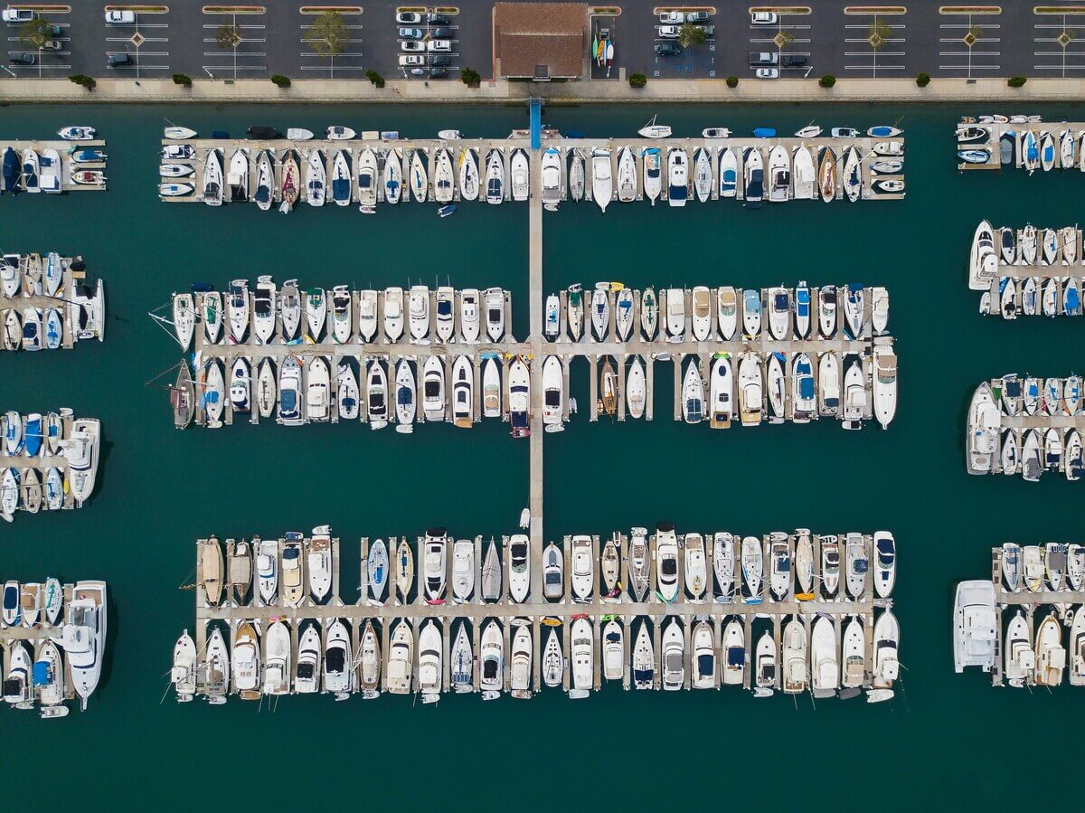 Aerial view of a marina with multiple rows of docked boats, showcasing ample seasonal boat moorage and a parking lot at the top of the image. Fill your empty slips fast with Marina Moorage