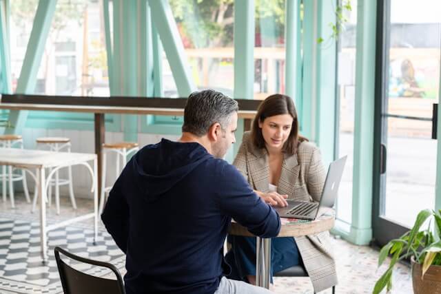 Two people sit at a small table, looking at a laptop screen together and discussing marina marketing solutions. Fill your empty slips fast with Marina Moorage