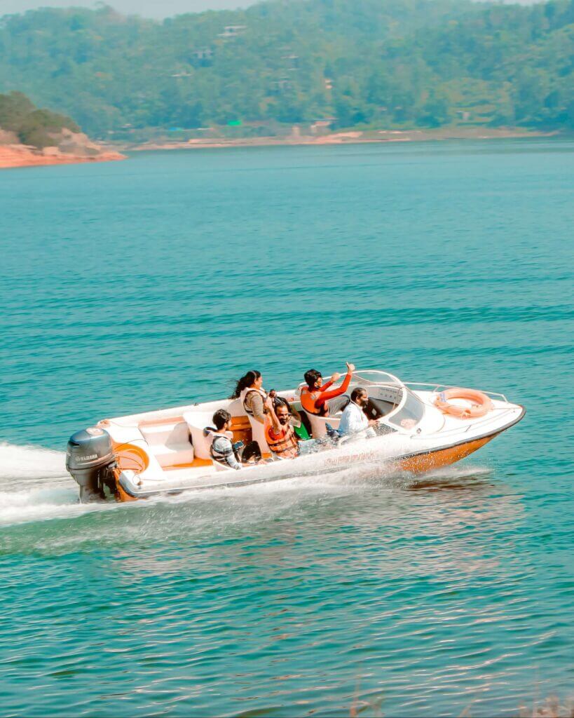 A group of people ride a white and orange speedboat across a calm blue lake with green hills in the background, passing by docks designed to fill marina slips. Fill your empty slips fast with Marina Moorage