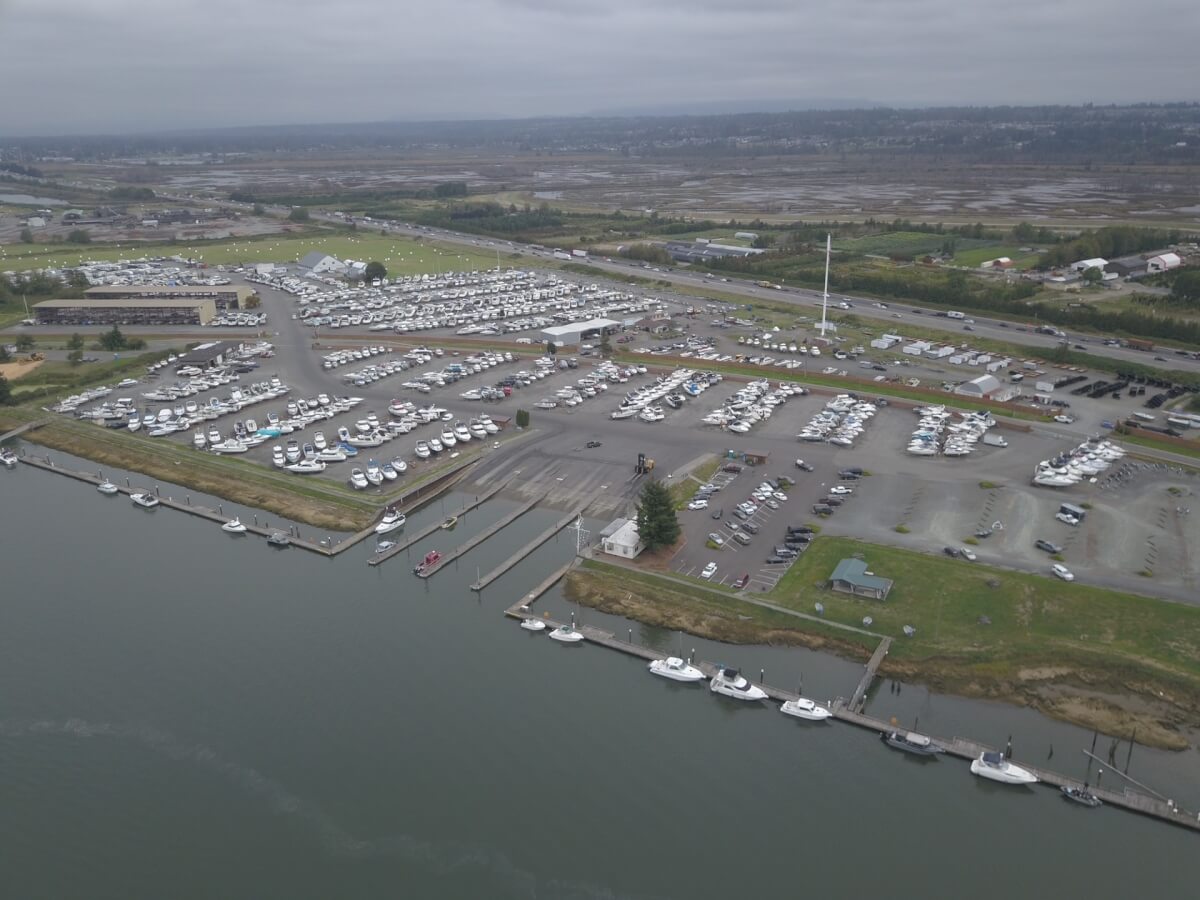 Aerial view of a large marina featuring extensive boat docking and moorage, with many parked boats, piers, parking lots, and grassy waterfront areas on a cloudy day. Fill your empty slips fast with Marina Moorage