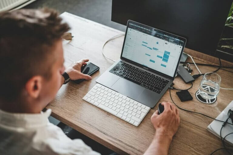 Person sitting at a desk using a laptop with marina slip listings open on the calendar, alongside a keyboard, mouse, two monitors, a phone, wallet, and a glass of water. Fill your empty slips fast with Marina Moorage